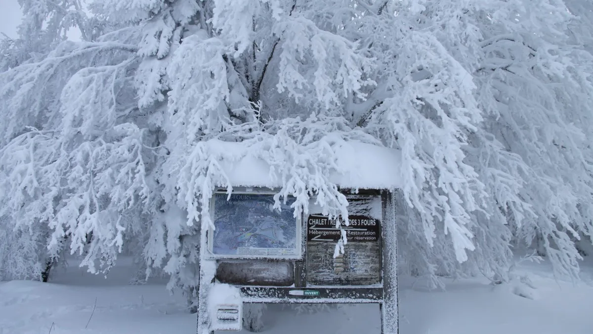 Information qui indique la direction de la Ferme-auberge des Trois Fours entourée de neige, au bord de la route des Crêtes dans les Vosges